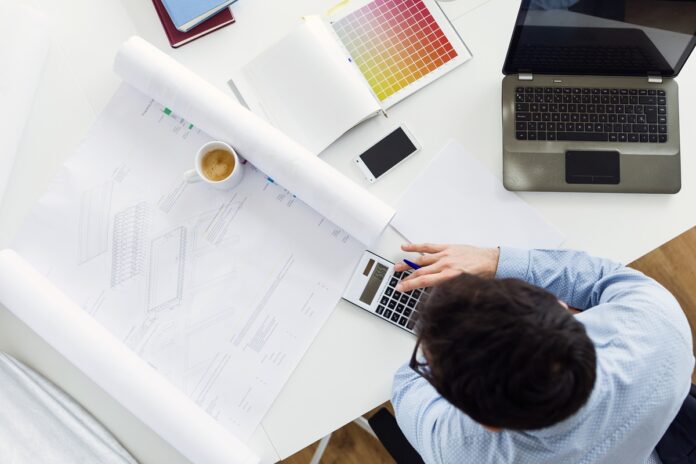 O que é plotagem de projetos? Homem analisa projeto plotado de arquitetura